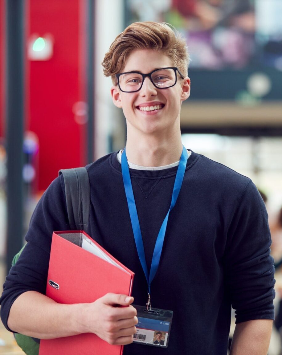 portrait of smiling male college student in busy communal campus building e1756285203815