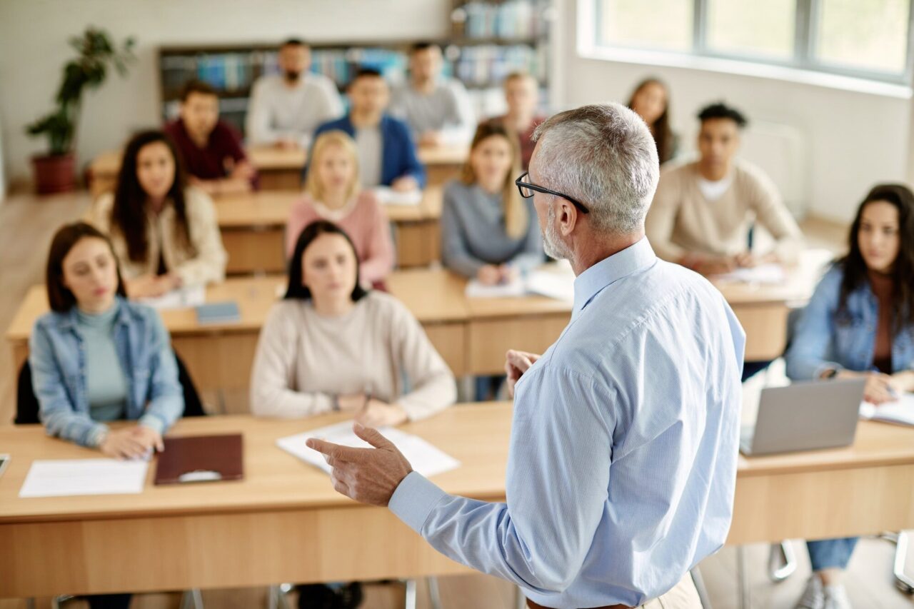rear view of mature teacher talking to his student during lecture at university classroom